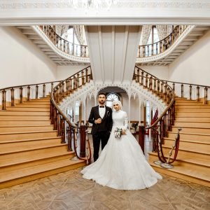 A sophisticated bride and groom stand on an ornate spiral staircase in a lavish interior setting.