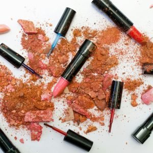 Colorful scattered makeup products including lipsticks and crushed powders on a white background.