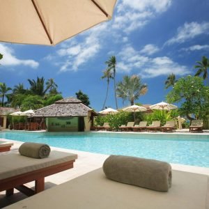 Experience ultimate relaxation at a sunlit tropical poolside resort featuring palm trees and blue skies.