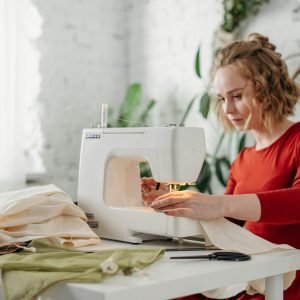 A woman in a red dress using a sewing machine at home, creating a handmade garment.