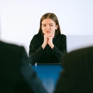A woman in a job interview facing two people at an office table, focusing intently.