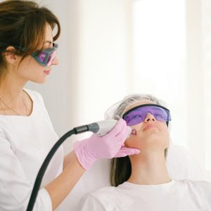 A cosmetologist performing laser treatment on a woman in a clinic setting.