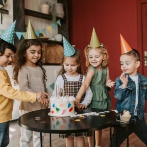 A joyful children's birthday party with colorful hats and a festive cake indoors.