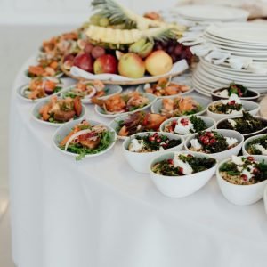 Bowls with bulgur and salads with fish served on white table with dishware and various ripe fruits during festive event