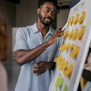 Confident African American man presenting business strategy using sticky notes on whiteboard.