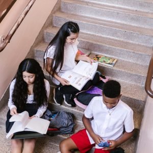 A group of teenagers studying and reading books while sitting on a staircase indoors.